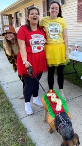 Two girls dressed up as Ketchup and Mustard with their dog dressed up as a hot dog