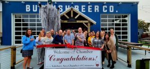 Large group of people standing outside cutting a large red ribbon