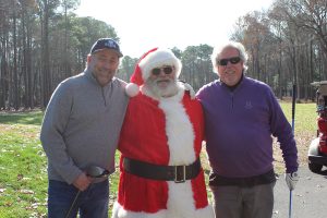 two grown man standing on a golf course next to Santa
