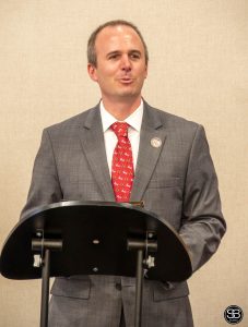 man in a gray suit and red tie standing at a podium