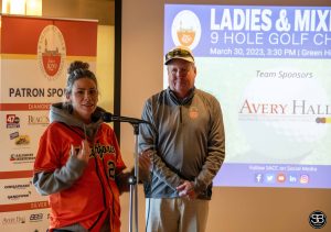 woman speaking in microphone with man standing next to her at golf event