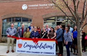 group of people holding congratulations banner outside coastal home care building