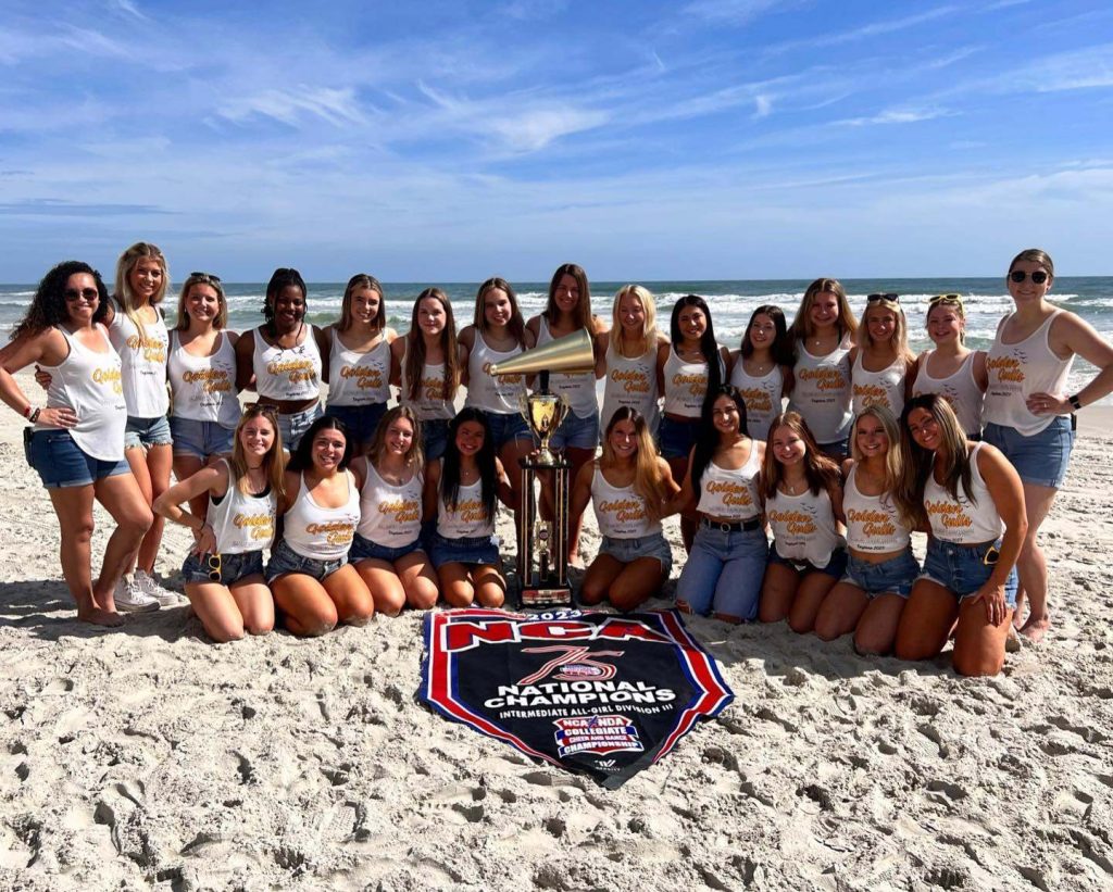 cheerleaders grouped together on beach with trophy