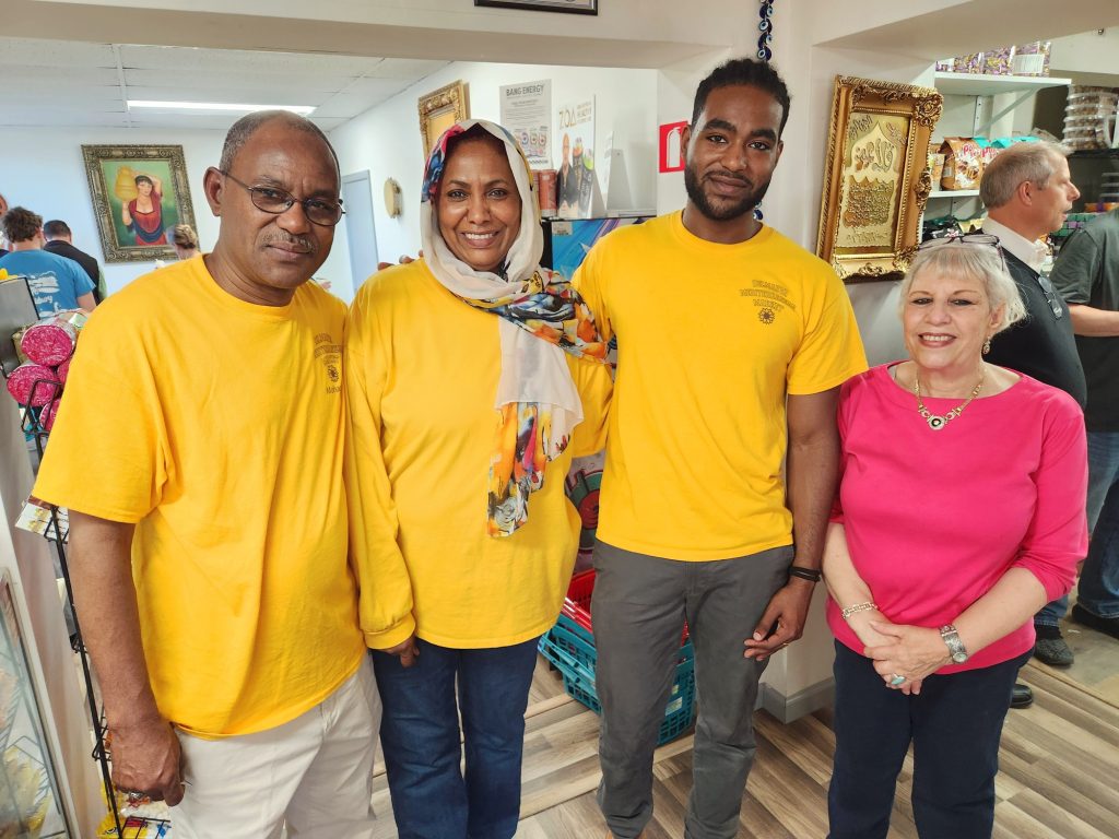 Two men in yellow shirts standing with a woman in yellow shirt and a woman in a pink shirt