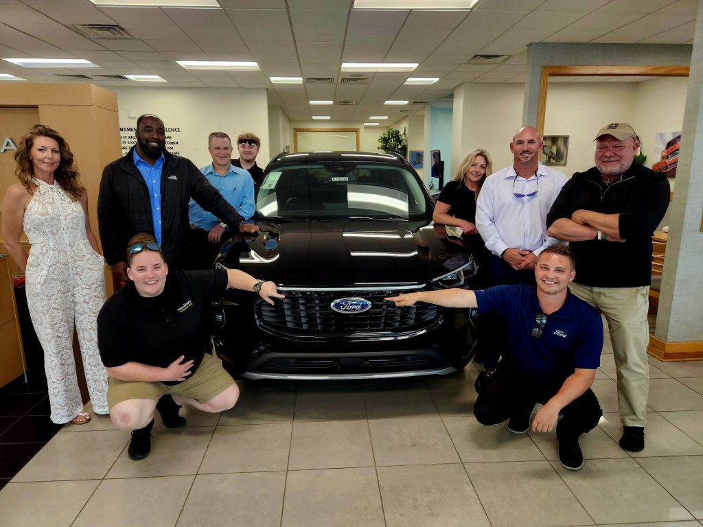 Group of people standing around a black Ford car