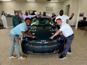 Group of people standing around a teal Kia car