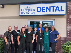 Group of people in surgical scrubs standing outside of a dental health care building sign