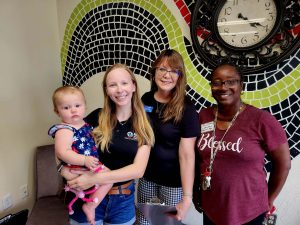 three ladies standing together with baby at event