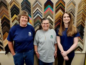 three ladies standing in front of frame border samples