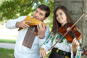 man and woman outside by tree holding instruments