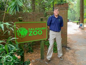 man standing next to salisbury zoo sign