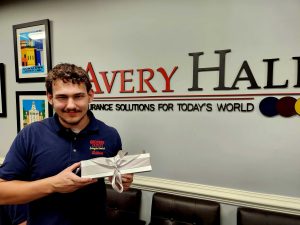 Man in a blue shirt holding a wrapped gift Avery Hall signage behind him