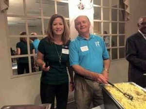 Woman in a green shirt standing next to a man in a blue shirt serving scrambled eggs at breakfast