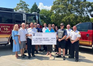 Group of people standing in front of a fire truck holidng a donation check