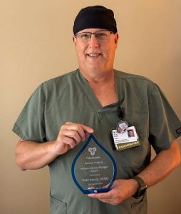 Todd Houck from TidalHealth Regional Hospital holding an award while wearing his scrubs