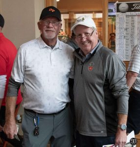 Man in a white hat and gray shirt standing with a man in white shirt and black hat