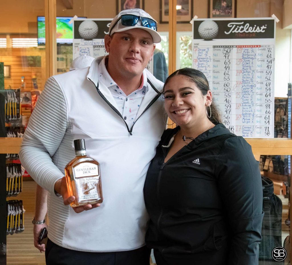 Man in a white jacket holding a bottle of gentleman jack standing with a woman in a black jacket