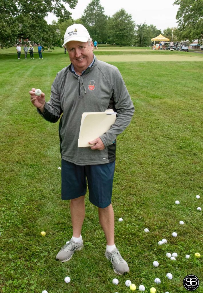 Man holding a golf ball and a folder standing on the golf course at a golf tournament