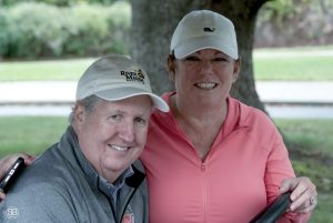 Man in a gray pullover posing with a woman in a pink shirt, both are smiling