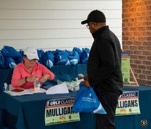 Man in a black jacket standing at a registration table holding a blue bag