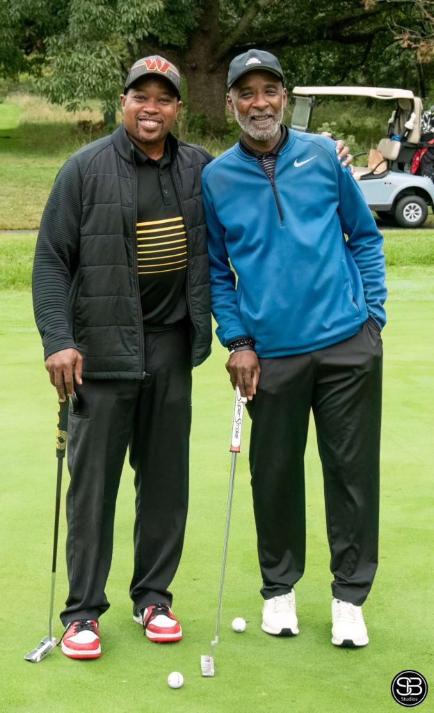 Two smiling gentleman standing on the golf course holding golf clubs