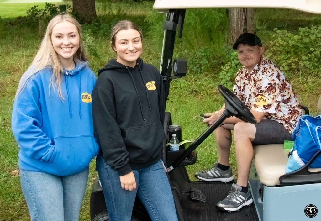 Man sitting in a golf cart, two women standing beside the golf cart