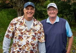 Man in a flowered shirt posing with a man in a blue jacket
