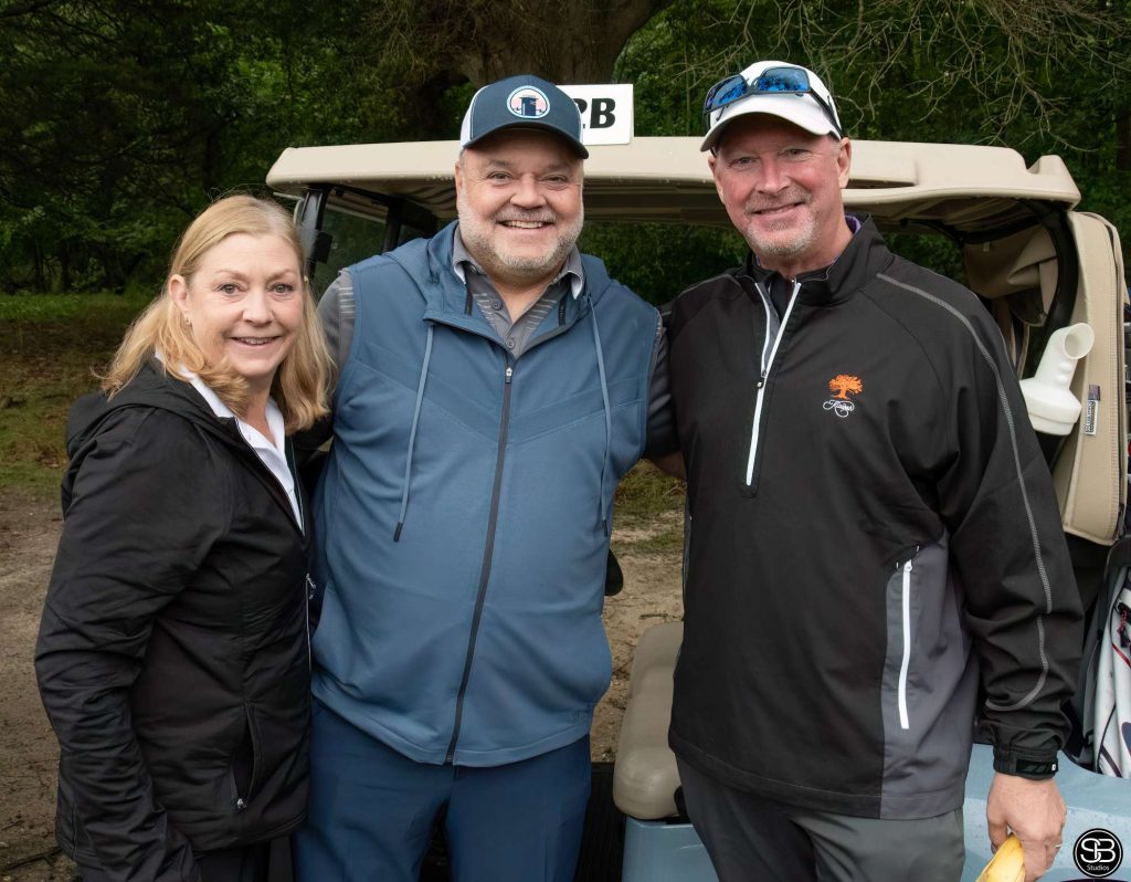 Three smiling golfers standing behind a golf cart