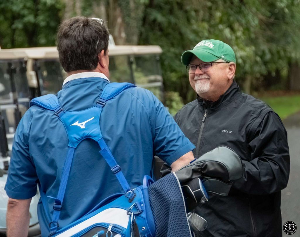 Man in a green Eagles hat smiling at a man carrying golf clubs