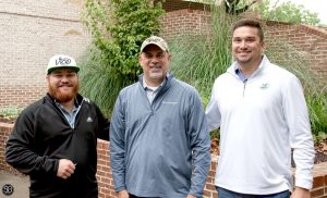 Three golfers standing by a brick wall