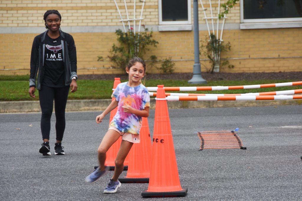 Young girl running around an orange traffic cone