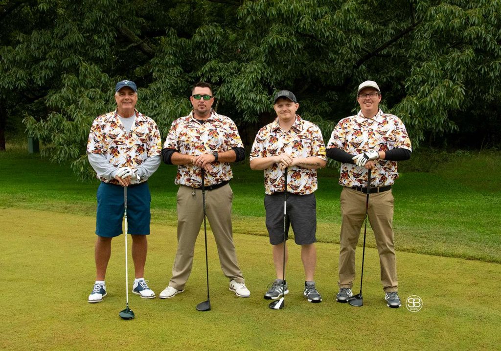 Golf Tournament Foursome standing on a golf course in flowered shirts all four holding golf clubs on a golf course