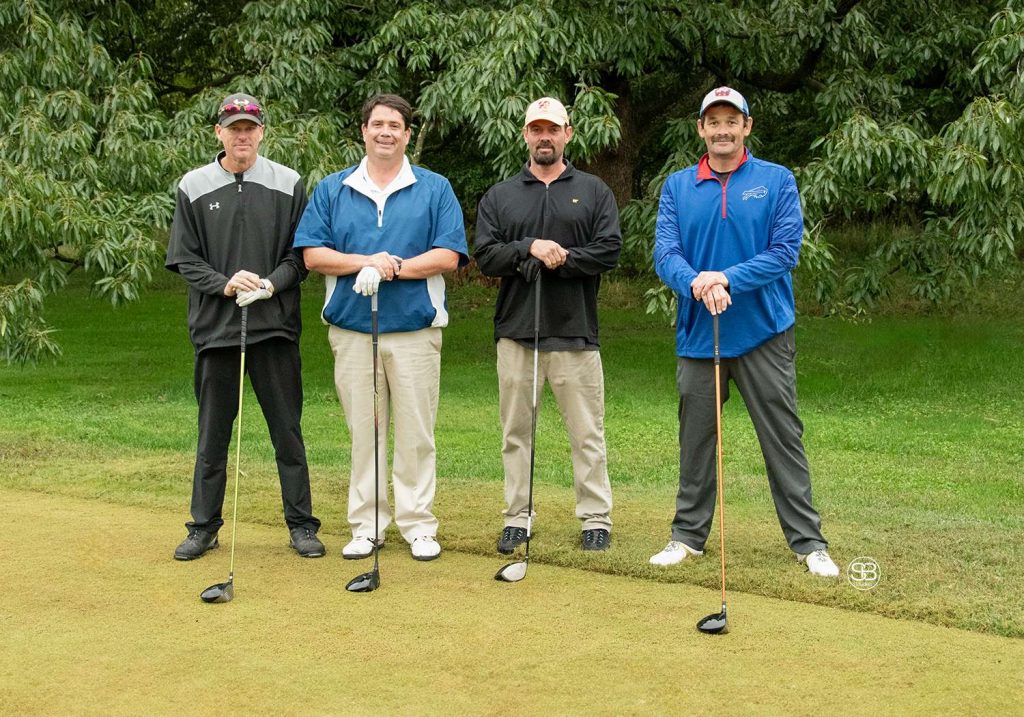 Golf Tournament Foursome standing on a golf course,, two men in blue jackets and two men in black jackets all four holding golf clubs
