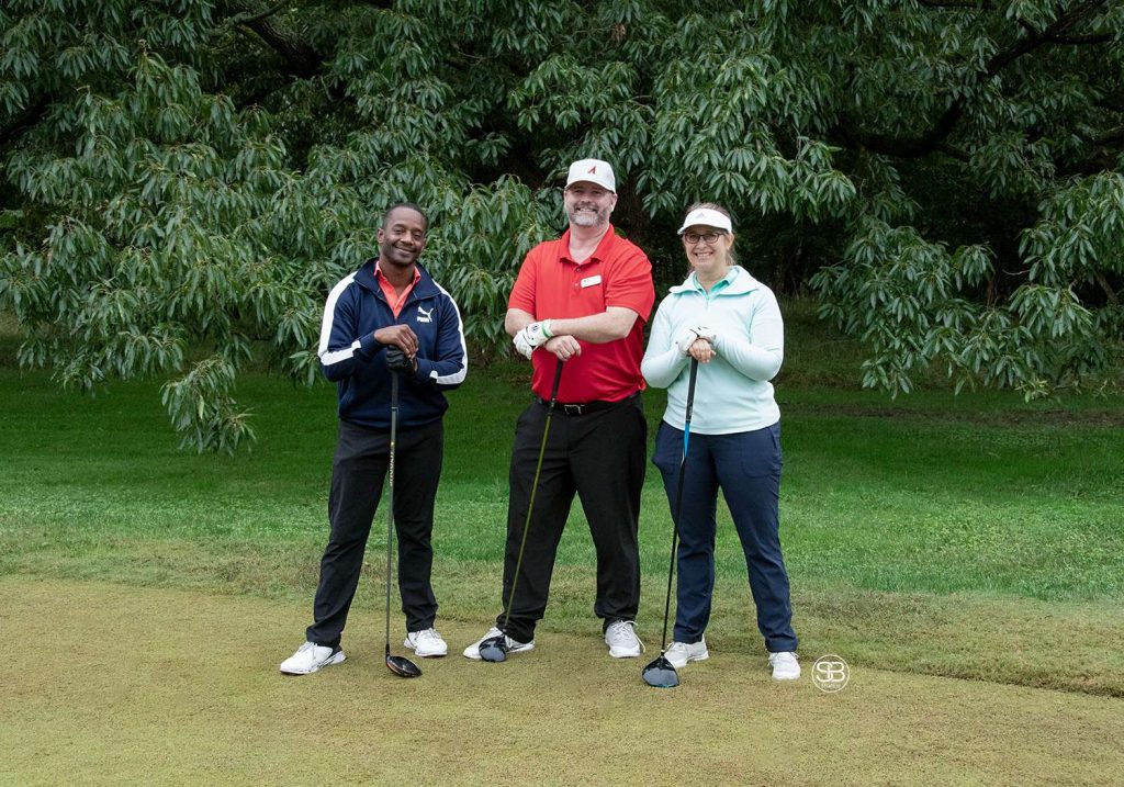Golf Tournament with two men and a woman standing on a golf course