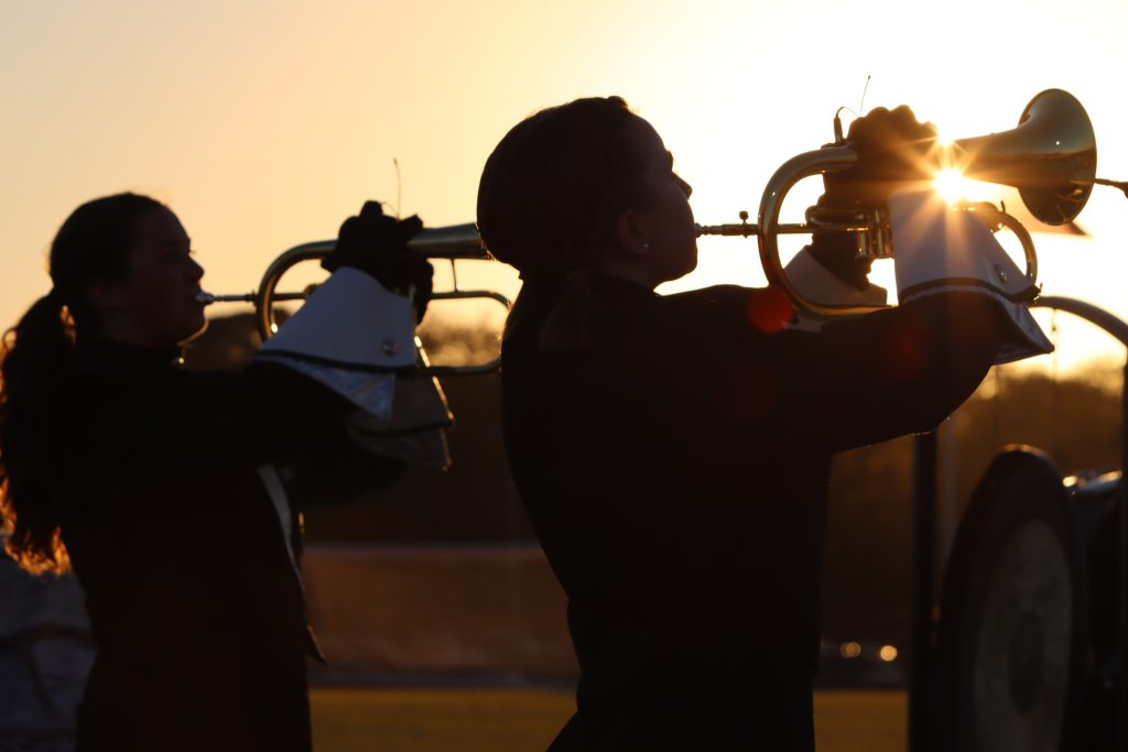 Marching band members playing their instruments in the sunset