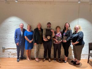 seven people lined up against a brick wall holding an award