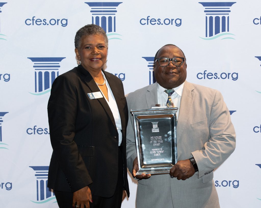 Man and woman in business attire standing together while holding a large award