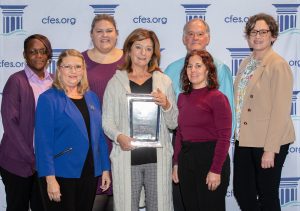 seven people gathered together holding a large award