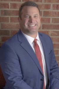 Headshot of a business man in a suit and tie against a brick wall