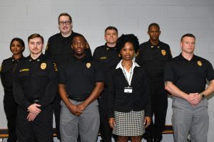 Several correction officers in black standing again a white wall