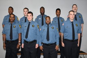 Several correctional officers in blue uniforms standing against a white wall