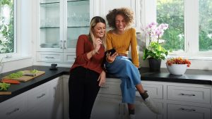 Two girls sitting on the kitchen counter looking at something on a mobile device