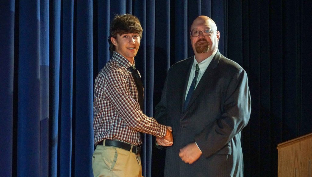 Young man in business attire shaking hands with an older gentleman as he accepts a scholarship award