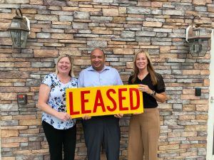 Three people holding a large wooden sign that says "Leased"