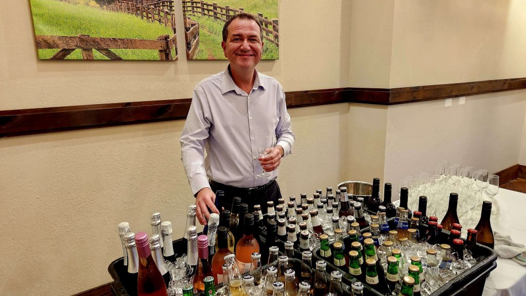 Smiling man behind a table of bottles of drinks