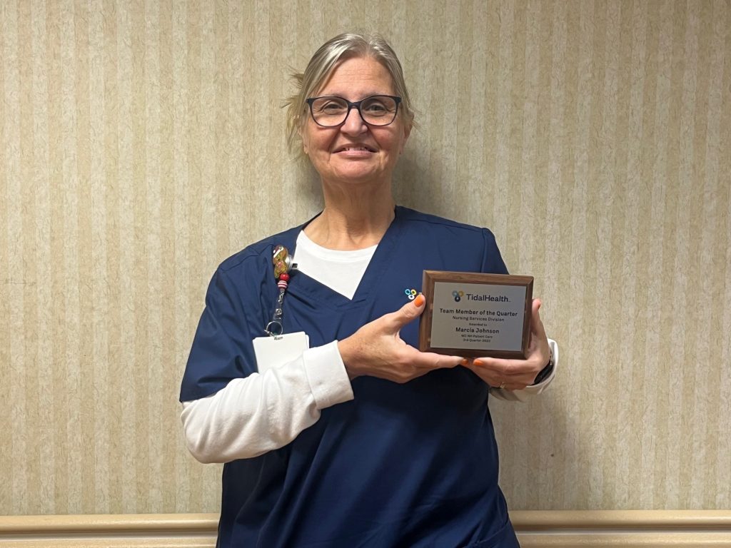 Headshot of a nurse in scrubs holding an award