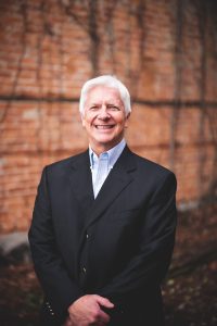 Headshot of Palmer Gillis in a suit against a brick background