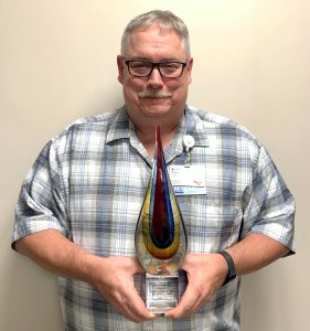 Dr. Robert Joyner holding an award against a blank wall