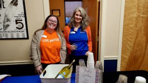 two women standing behind the wine table at an event