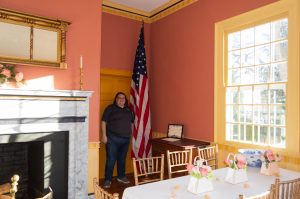 Poplar Hill Mansion Curator Sarah Meyers stands by the flag that was donated by the Samuel Chase Chapter of the National Society Daughters of the American Revolution, which helps show the large size of the flag.
